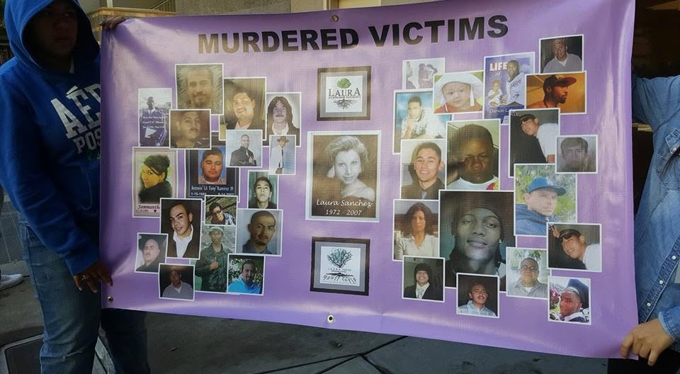 A SCARED STIFF community memorial board titled MURDERED VICTIMS, covered in photographs of young people lost to gun violence